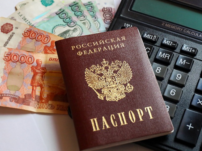 На изображении паспорт РФ, калькулятор и купюры номиналом 5000 рублей. Предметы лежат на белой поверхности..