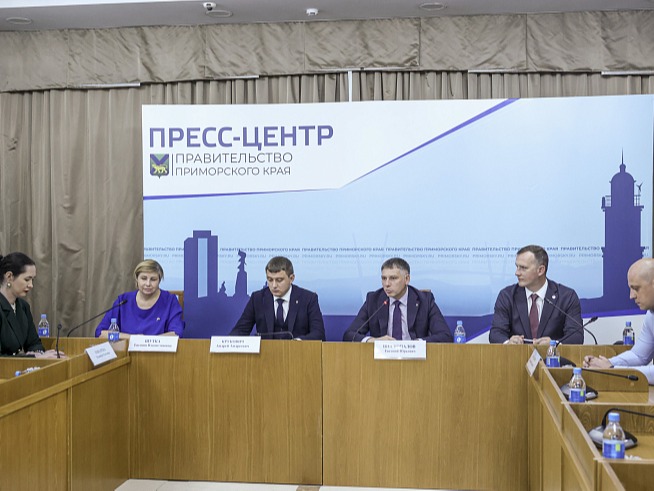 На изображении пресс-конференция в пресс-центре правительства Приморского края. За столом сидят пять человек, перед ними микрофоны и таблички с именами..